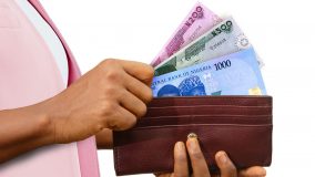 fair Female Hand Holding brown Purse With Nigerian naira notes, hand removing money out of purse isolated on white background